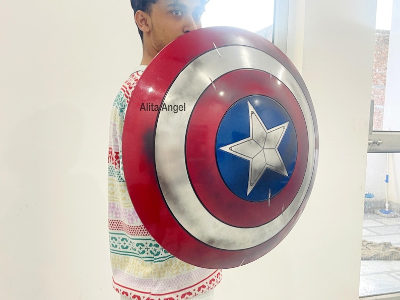 May include: A Captain America shield with a red, white, and blue color scheme. The shield features a white star on a blue circle, surrounded by white and red concentric rings. The shield is a prop or collectible.