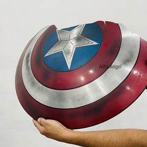 K&ouml;nnte beinhalten: Ein Captain America Schild-Requisite mit einem rot, wei&szlig; und blau Farbschema. Das Schild hat einen zentralen blauen Kreis mit einem silbernen Stern, umgeben von wei&szlig;en und roten Ringen. Das Schild wird von einer Person gehalten.
