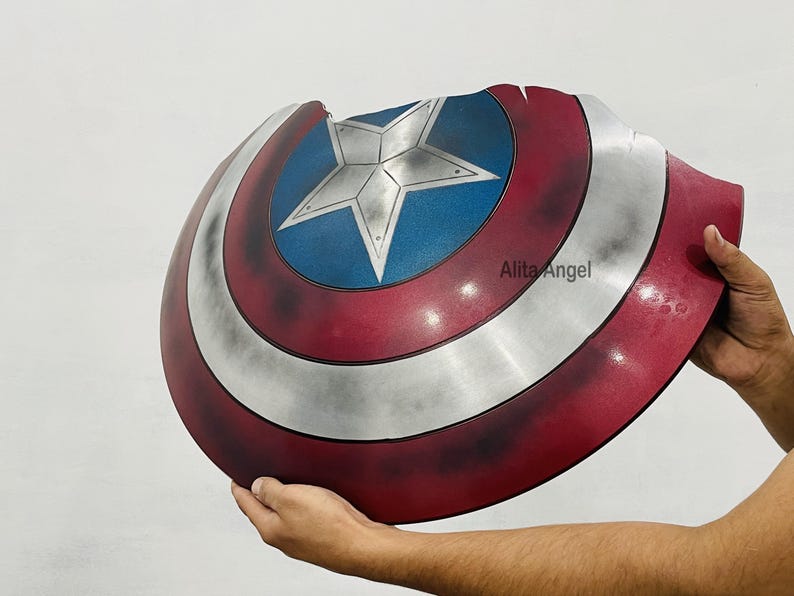 K&ouml;nnte beinhalten: Ein Captain America Schild-Requisite mit einem rot, wei&szlig; und blau Farbschema. Das Schild hat einen zentralen blauen Kreis mit einem silbernen Stern, umgeben von wei&szlig;en und roten Ringen. Das Schild wird von einer Person gehalten.