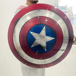 May include: A round shield with a red, white, and blue color scheme. The shield features a central blue circle with a white star, surrounded by concentric rings of silver, white, and red. The shield is a prop from a superhero movie.