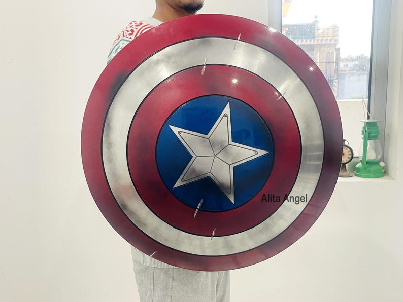May include: A round shield with a red, white, and blue color scheme. The shield features a central blue circle with a white star, surrounded by concentric rings of silver, white, and red. The shield is a prop from a superhero movie.