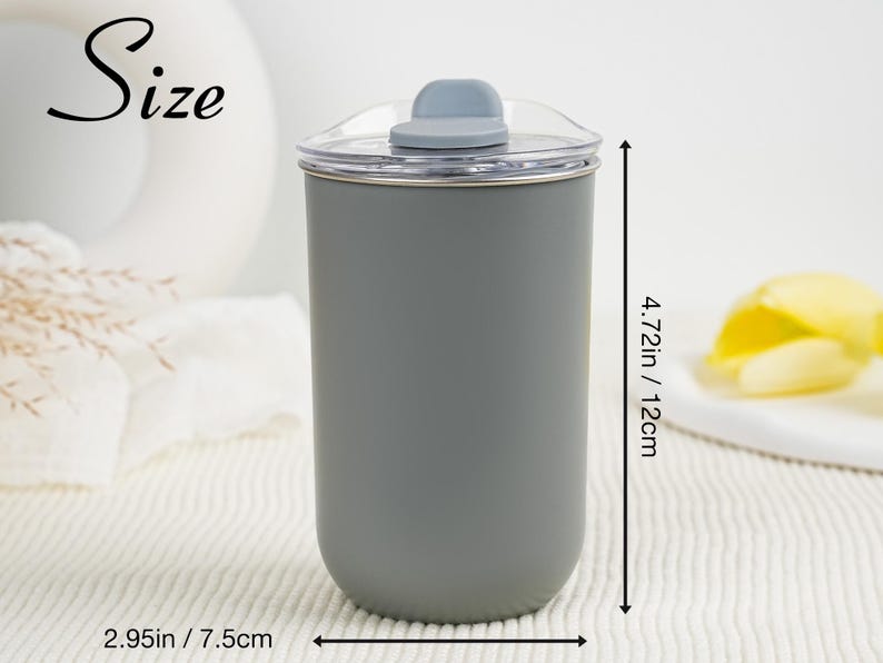 May include: A gray tumbler with a clear lid and a gray flip-top closure. The tumbler is 4.72 inches (12 cm) tall and 2.95 inches (7.5 cm) wide. The word "Size" is written in cursive on the upper left.