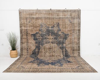 May include: Large, rectangular area rug with a distressed, vintage appearance. The rug features a central design in shades of navy blue and brown, with intricate patterns and a faded look. The rug is displayed against a white background.
