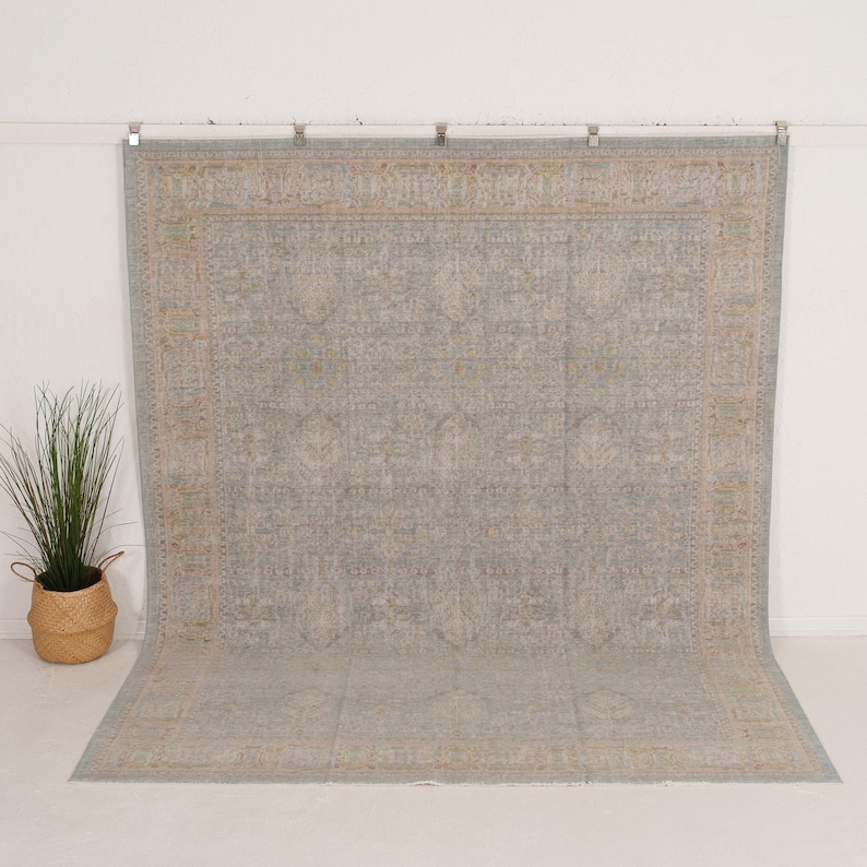 May include: A large rectangular area rug featuring a muted light blue and gray base color with intricate, faded tan and beige floral and geometric patterns throughout the center and a wide, detailed border framing the entire design.