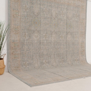 May include: A large area rug featuring a faded, intricate pattern in shades of light blue, beige, and soft gray. The design includes a central medallion and a wide, detailed border with repeating geometric and floral motifs across the surface.