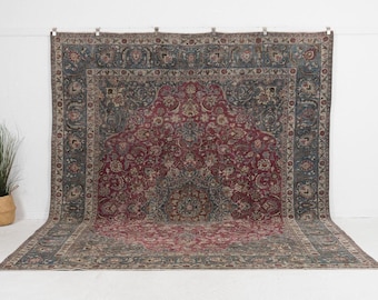 May include: A large, rectangular rug with an intricate floral design. The rug features a central field of deep red, surrounded by a border of blue-gray and beige. The pattern includes stylized flowers and leaves, creating a classic, ornate look.