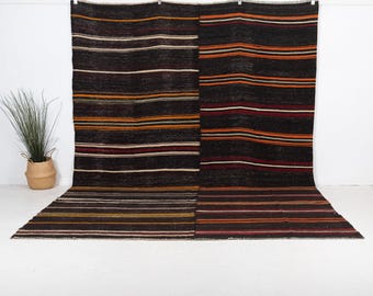 May include: A large rectangular area rug featuring a dark brown base with horizontal stripes in shades of orange, red, white, and yellow. The rug is displayed hanging vertically and extending across the floor, showcasing a consistent striped pattern.