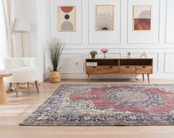 May include: A large, rectangular, vintage-style rug with a central medallion design in shades of red, blue, and cream. The rug is placed on a light wood floor in a room with white walls and wooden furniture. Decorative wall art is visible.