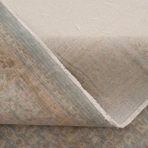 May include: A folded area rug showing a patterned top surface in muted shades of blue, beige, and brown, contrasted with a plain, light beige woven backing. The fabric texture is visible, highlighting the weave of the rug's underside and edges.