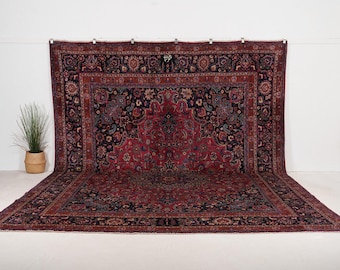 May include: A large rectangular area rug featuring a complex floral and paisley pattern in deep shades of red, navy blue, and cream. The design includes a prominent central medallion surrounded by intricate borders and a dense botanical motif.