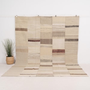 May include: A large, rectangular rug with a patchwork design. The rug features a neutral colour palette of beige, cream, and brown tones. The design is composed of rectangular blocks with horizontal stripes. The rug is displayed against a white background.