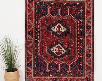 Puede incluir: Una alfombra rectangular con una paleta de colores rojo intenso y azul marino con intrincados patrones geométricos. El diseño incluye dos medallones centrales en forma de diamante en crema y rojo, rodeados por bordes ornamentados y motivos florales.