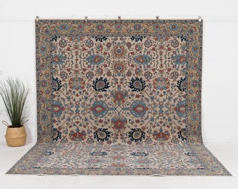 May include: A large rectangular area rug featuring a beige background with an intricate floral and vine pattern in shades of navy blue, terracotta red, and light blue. The rug has a wide decorative border with repeating floral motifs.