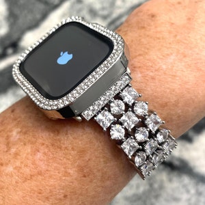 May include: A silver Apple Watch with a diamond-encrusted band and case. The watch face is black with the Apple logo displayed.