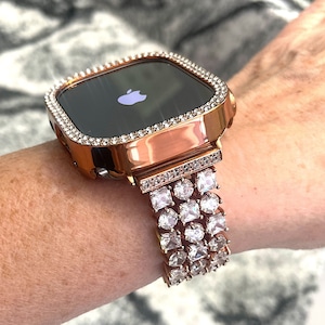 May include: A rose gold Apple Watch with a diamond-encrusted case and band. The watch face is black and displays the Apple logo.