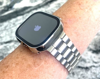 以下が含まれることがあります： ステンレス製のバンドが付いたシルバーのApple Watch。時計の文字盤は黒で、Appleのロゴが表示されています。