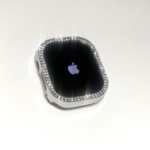 Op de afbeelding: Een zilveren Apple Watch met een heldere, glinsterende diamant-achtige bezel. Het horloge-scherm is zwart en toont het Apple-logo.