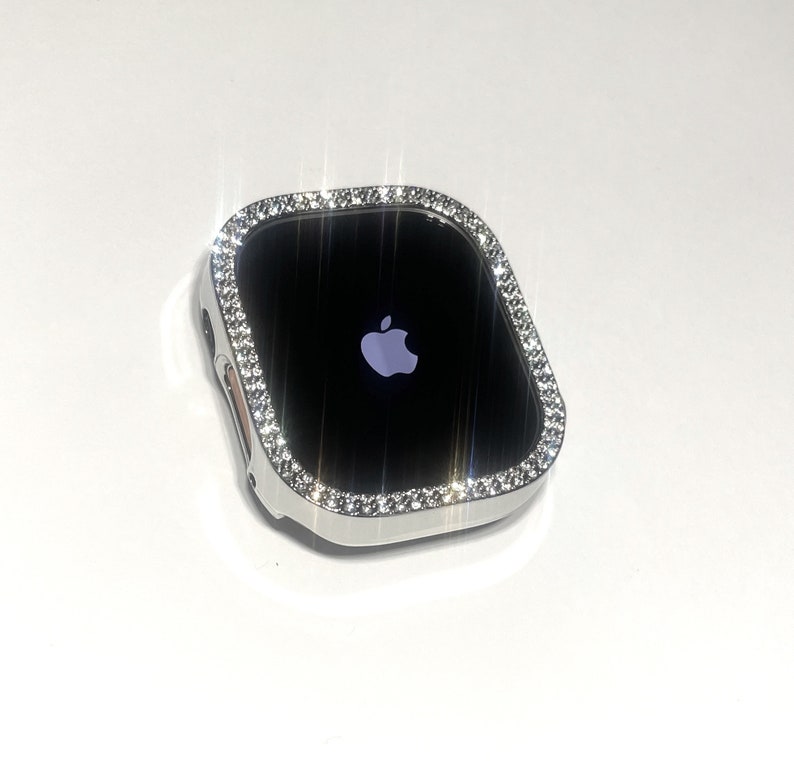 Op de afbeelding: Een zilveren Apple Watch met een heldere, glinsterende diamant-achtige bezel. Het horloge-scherm is zwart en toont het Apple-logo.