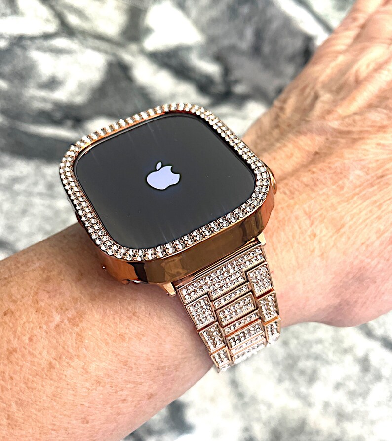 Puede incluir: Un Apple Watch de oro rosa con una banda y un bisel engastados con diamantes. La esfera del reloj es negra y presenta el logotipo de Apple.