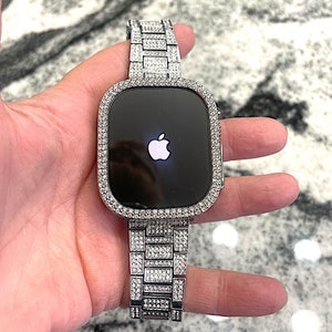 Op de afbeelding: Een zilveren Apple Watch met een band en bezel bezet met diamanten. De wijzerplaat van het horloge is zwart en toont het Apple-logo.