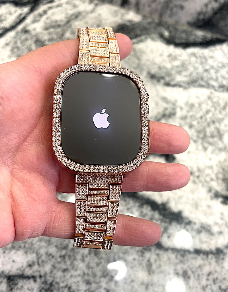 Puede incluir: Un Apple Watch de oro rosa con una banda y un bisel engastados con diamantes. La esfera del reloj es negra y presenta el logotipo de Apple.
