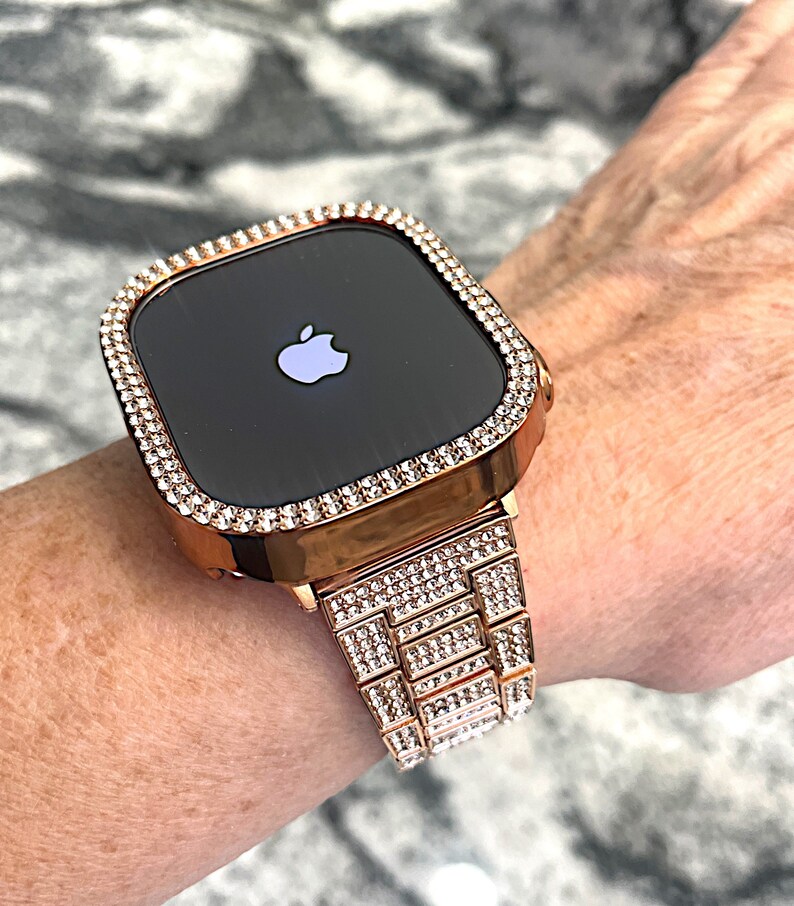 Puede incluir: Un Apple Watch de oro rosa con una banda y un bisel engastados con diamantes. La esfera del reloj es negra y presenta el logotipo de Apple.