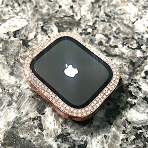 Puede incluir: Una esfera de reloj Apple de oro rosa con un bisel engastado con diamantes. La esfera del reloj es negra y presenta el logotipo de Apple.