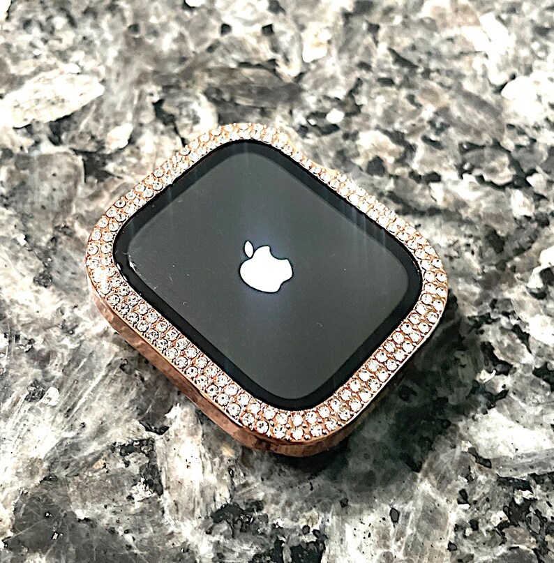 Puede incluir: Una esfera de reloj Apple de oro rosa con un bisel engastado con diamantes. La esfera del reloj es negra y presenta el logotipo de Apple.