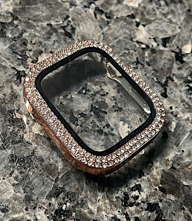 Puede incluir: Una carcasa de Apple Watch de oro rosa con un protector de pantalla transparente y un bisel incrustado con cristales que parecen diamantes.