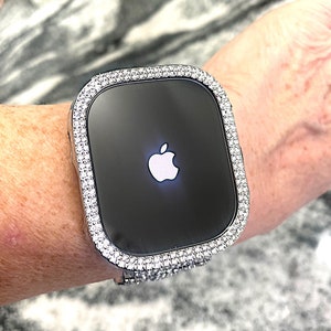 Op de afbeelding: Een zilveren Apple Watch met een bezel bezet met diamanten. De wijzerplaat van het horloge is zwart en toont het Apple-logo.