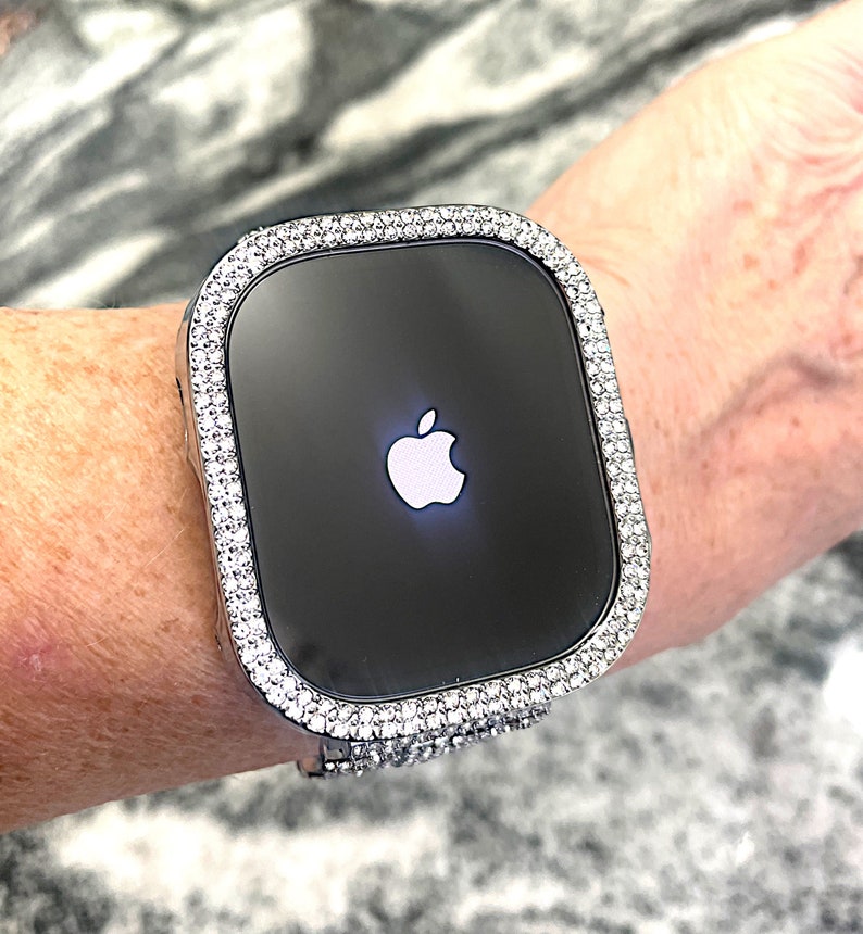 Op de afbeelding: Een zilveren Apple Watch met een bezel bezet met diamanten. De wijzerplaat van het horloge is zwart en toont het Apple-logo.