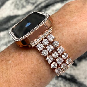 May include: A rose gold Apple Watch with a diamond-encrusted band and bezel. The watch face is black and shows the Apple logo.