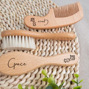 May include: A wooden baby grooming set featuring a brush, comb, and a smaller brush. The set includes the name "Grace" and a giraffe illustration. The items are made of light-colored wood and are arranged on a woven surface.