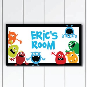 以下が含まれることがあります： 青い文字で「Eric's Room」と書かれた黒い額縁の看板。看板は、さまざまな表情をしたカラフルな漫画のモンスターで飾られています。