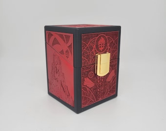 May include: A black and red box with a gold clasp. The red panels feature intricate etched designs, including a castle and geometric patterns. The box is cube-shaped and appears to be made of wood or a similar material.