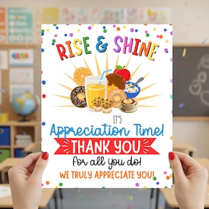 Könnte beinhalten: Ein farbenfrohes Poster mit den Worten "Rise & Shine" und "Appreciation Time! Thank You". Das Bild zeigt Illustrationen von Frühstückszutaten wie Donuts, Saft und Obst. Das Poster wird von einer Person in einem Klassenzimmer gehalten.