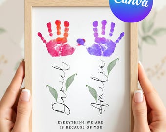 May include: A framed print featuring two handprints in pink and purple, with the names "Daniel" and "Amelia" below. The text "Everything we are is because of you" is also included. The frame is light brown.