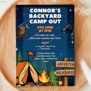 Könnte beinhalten: Eine marineblaue Einladung für Connors Backyard Camp Out mit einer Eule, einem Zelt, einem Lagerfeuer und einem Fernglas. Die Einladung enthält Datum, Uhrzeit, Ort und RSVP-Informationen. Die Einladung liegt auf einem Holztablett.