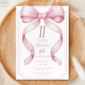 Puede incluir: Una invitación de cumpleaños rosa con un gran diseño de lazo y cinta. La invitación dice "11º Cumpleaños de Amelia" e incluye la fecha, la hora y el lugar. La invitación está sobre un fondo blanco.