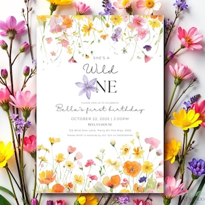 Può includere: Un biglietto d'invito bianco con illustrazioni floreali e il testo "She's a Wild One" e "Bella's first birthday". Il biglietto è circondato da fiori colorati rosa, gialli e viola.