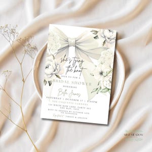 May include: A bridal shower invitation featuring a large, elegant bow and floral accents. The invitation includes the text "she's tying the knot" and details for the event, including the honoree's name, date, time, and location.