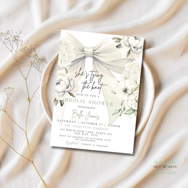 May include: A bridal shower invitation featuring a large, elegant bow and floral accents. The invitation includes the text "she's tying the knot" and details for the event, including the honoree's name, date, time, and location.