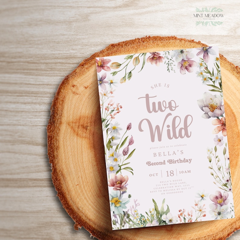 May include: A floral-themed birthday invitation with the text "She is Two Wild" in a cursive font. The invitation is surrounded by watercolor flowers in shades of pink, purple, and white. The invitation is on a wooden surface.