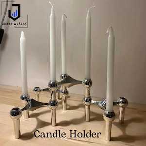 May include: A silver metal candle holder with six white candles. The candle holder has a modern design with spherical accents and a geometric base. The text "Candle Holder" is displayed at the bottom of the image.