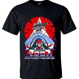 Puede incluir: Camiseta negra con un gráfico de la serie de anime Macross. El diseño incluye un fondo rojo y blanco en forma de estrella, un robot con una pistola y un piloto en una cabina. La palabra "MACROSS" se muestra en blanco.
