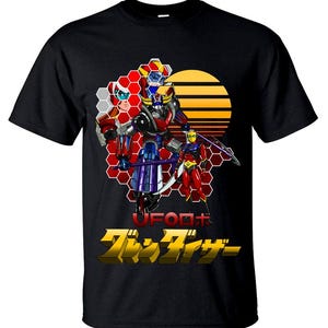 Puede incluir: Camiseta negra con un gráfico colorido de un robot y dos figuras contra un fondo de puesta de sol. El diseño incluye texto japonés y las palabras "UFO Robot". La obra de arte está enmarcada por un patrón de panal rojo y blanco.