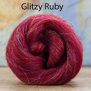 May include: A close-up of a deep red wool roving with iridescent fibers. The roving is rolled into a ball shape. The text "Glitzy Ruby" is written above the roving.