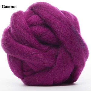 Puede incluir: Primer plano de una bola de lana de color Damson. La lana es de un tono p&uacute;rpura intenso y rico, enrollada en forma esf&eacute;rica. La textura de la lana es suave y esponjosa, con fibras visibles. La palabra "Damson" est&aacute; en la esquina superior izquierda.