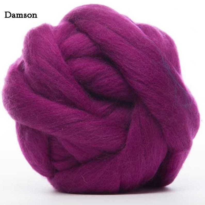 Puede incluir: Primer plano de una bola de lana de color Damson. La lana es de un tono p&uacute;rpura intenso y rico, enrollada en forma esf&eacute;rica. La textura de la lana es suave y esponjosa, con fibras visibles. La palabra "Damson" est&aacute; en la esquina superior izquierda.