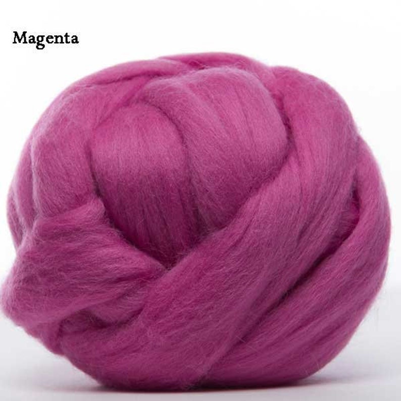 Puede incluir: Primer plano de una bola de lana de color magenta. El texto "Magenta" est&aacute; en la esquina superior izquierda. La lana est&aacute; densamente empaquetada y parece suave y esponjosa, ideal para proyectos de arte textil como fieltro con aguja o fieltro h&uacute;medo.